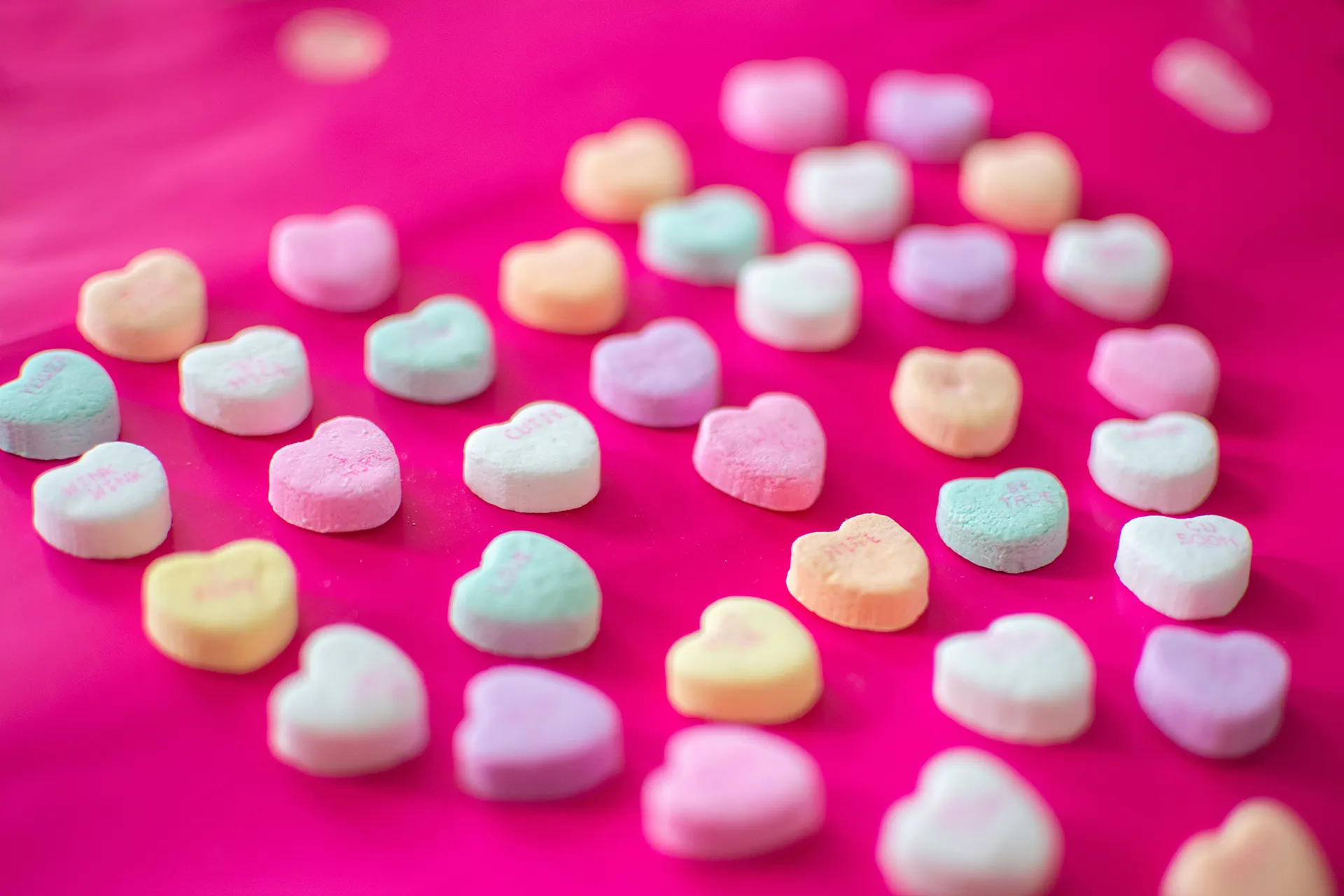 Candy hearts on a pink background, arranged in a heart shape